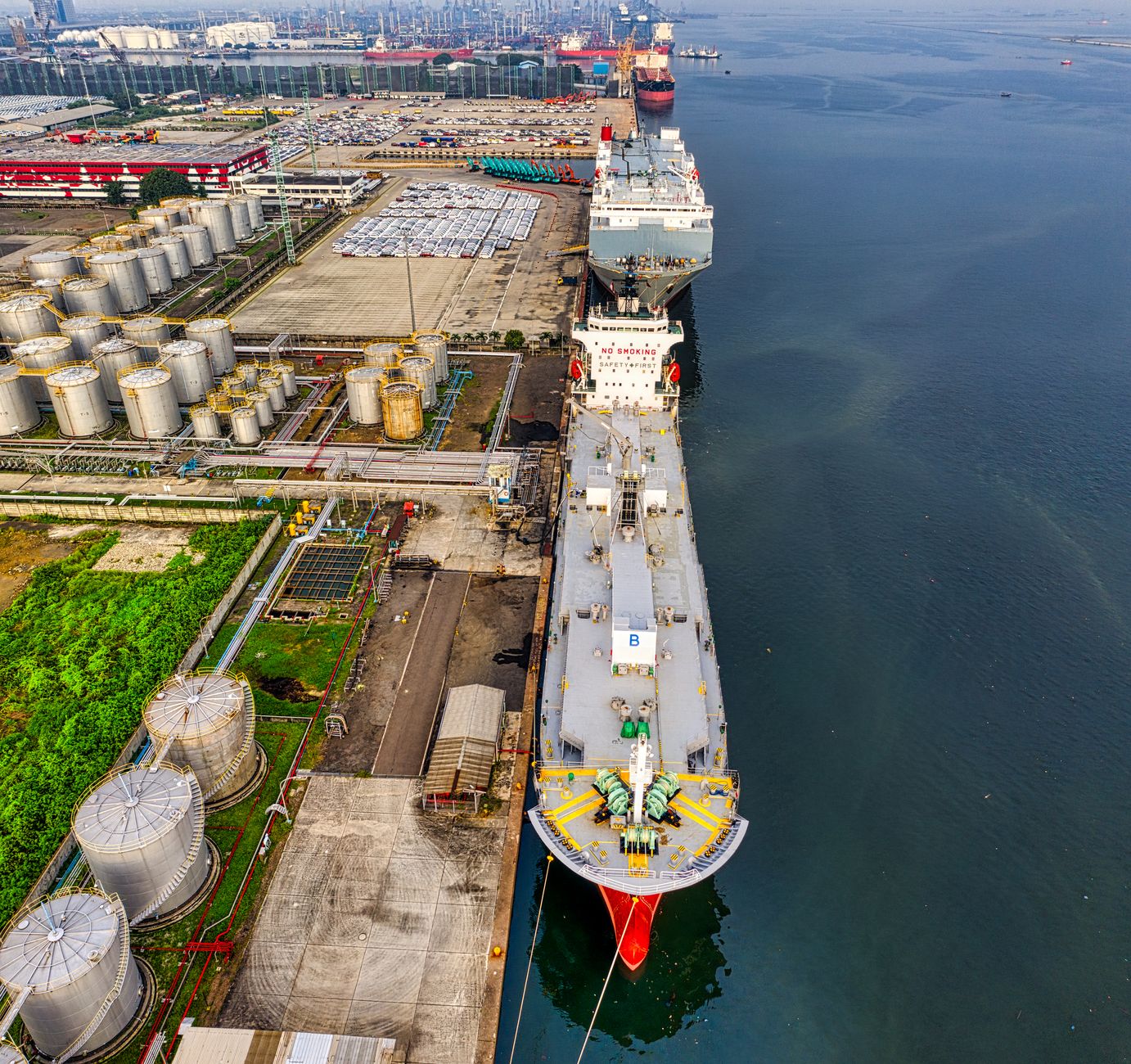 Vue aérienne d’un grand navire amarré le long d’un quai industriel à côté de réservoirs de stockage.